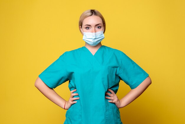 Vorderansicht der jungen Ärztin im medizinischen Hemd und in der Maske auf gelber Wand
