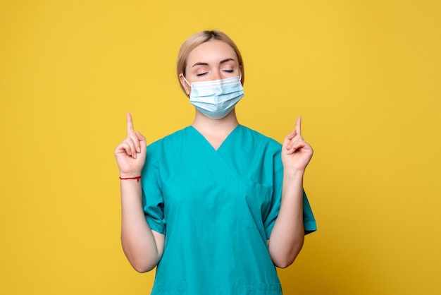 Vorderansicht der jungen Ärztin im medizinischen Hemd und in der Maske auf gelber Wand