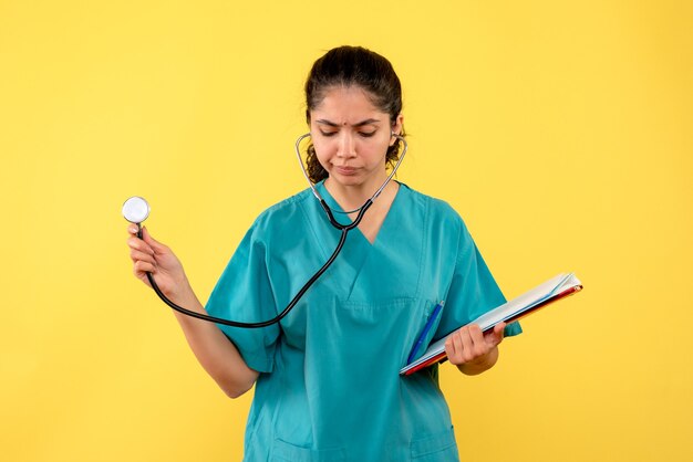 Vorderansicht der jungen Ärztin mit Stethoskop und Dokumenten auf gelber Wand
