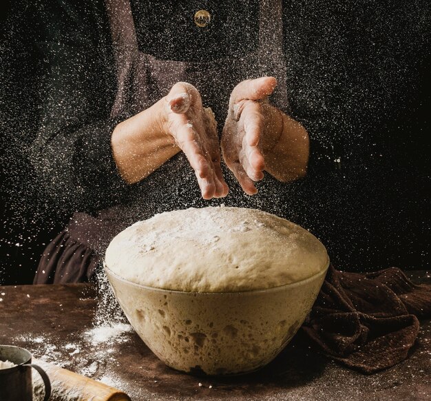 Vorderansicht der Köchin, die ihre Hände mit Mehl abstaubt, bevor Pizzateig behandelt wird