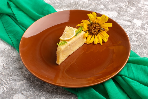 Vorderansicht der köstlichen Kuchenscheibe mit Zitrone innerhalb der braunen Platte auf dem hellen Schreibtischkuchen