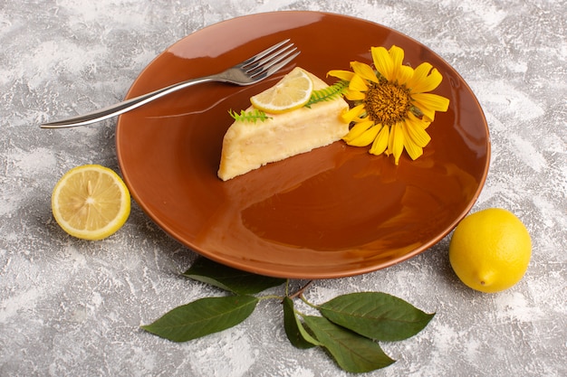 Vorderansicht der köstlichen Kuchenscheibe mit Zitrone innerhalb der braunen Platte auf der hellen Oberfläche