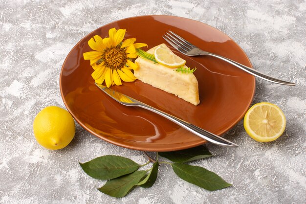 Vorderansicht der köstlichen Kuchenscheibe mit Zitrone innerhalb der braunen Platte mit Gabeln auf der hellen Oberfläche