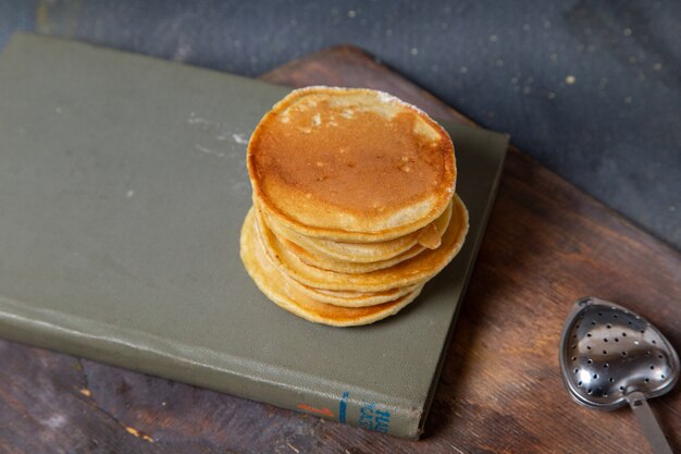 Vorderansicht der köstlichen Pfannkuchen auf dem hölzernen Schreibtisch des Heftes und der grauen Oberfläche