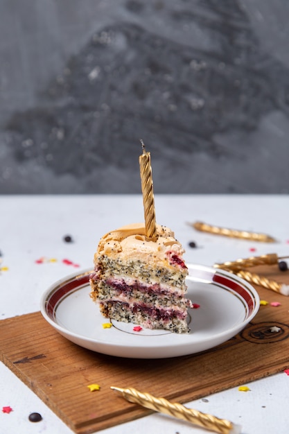 Vorderansicht der Kuchenscheibe innerhalb Platte mit Kerzen auf dem hellen Schreibtisch