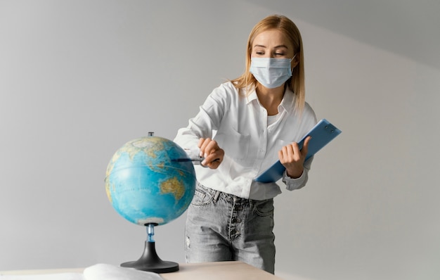 Vorderansicht der Lehrerin im Klassenzimmer mit Zwischenablage, die auf Globus zeigt