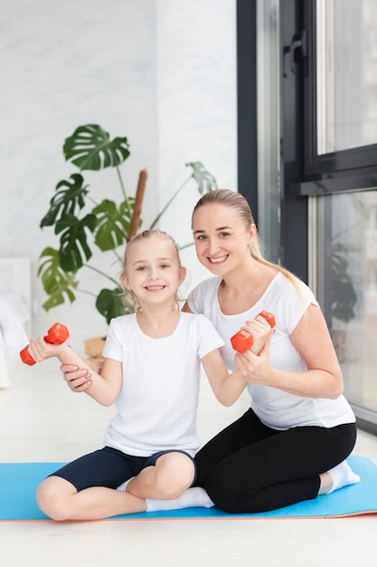 Kostenloses Foto vorderansicht der mutter, die mit tochter und gewichten aufwirft