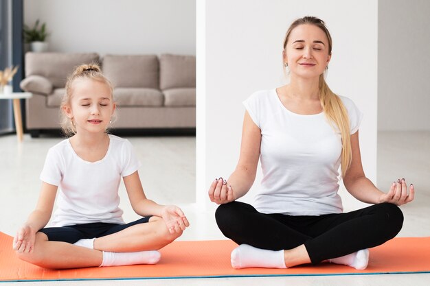 Vorderansicht der Mutter, die Yoga mit Tochter zu Hause tut