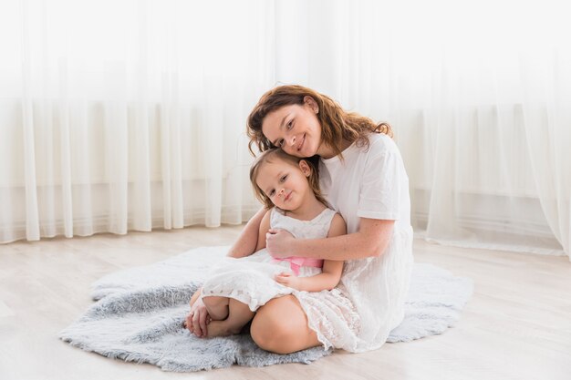 Vorderansicht der Mutter mit ihrem Kindermädchen, das auf flaumigem Teppich im Haus sitzt