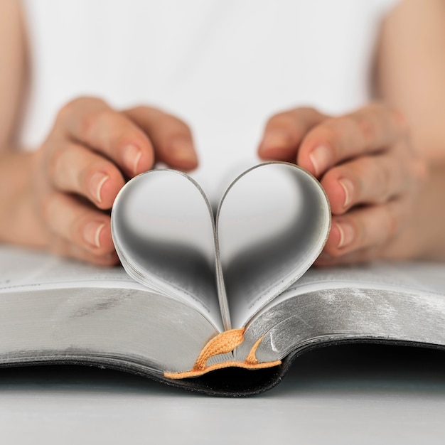 Vorderansicht der Person, die Herz von den heiligen Buchseiten macht
