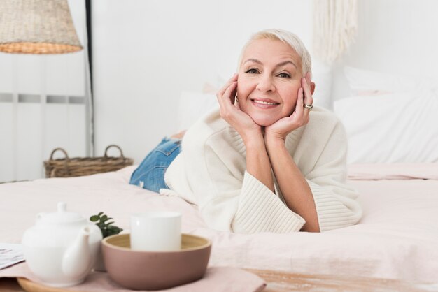 Vorderansicht der reifen glücklichen Frau, die im Bett lächelt und aufwirft