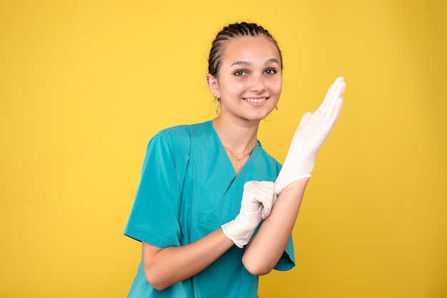 Vorderansicht der Ärztin, die Handschuhe auf gelber Wand trägt