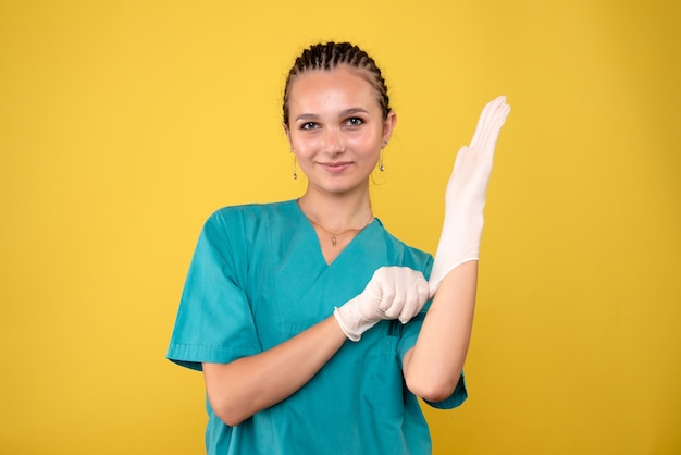 Vorderansicht der Ärztin, die spezielle Handschuhe auf gelber Wand trägt