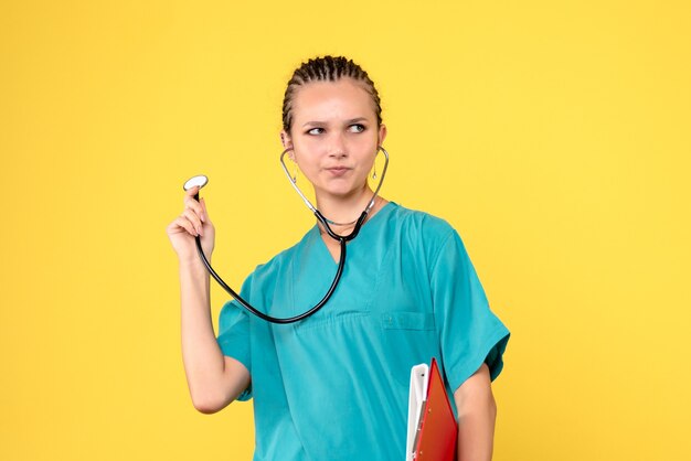Vorderansicht der Ärztin im medizinischen Anzug mit Stethoskop und Analyse auf gelber Wand