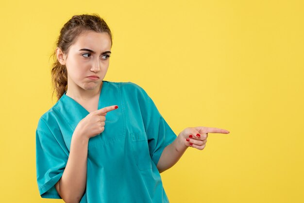 Vorderansicht der Ärztin im medizinischen Anzug traurig auf einer gelben Wand