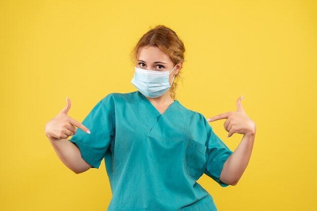 Vorderansicht der Ärztin im medizinischen Anzug und in der Maske auf gelber Wand