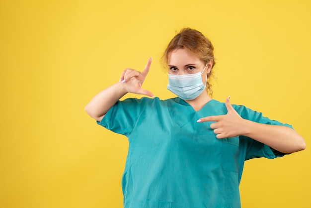 Vorderansicht der Ärztin im medizinischen Anzug und in der sterilen Maske auf gelber Wand