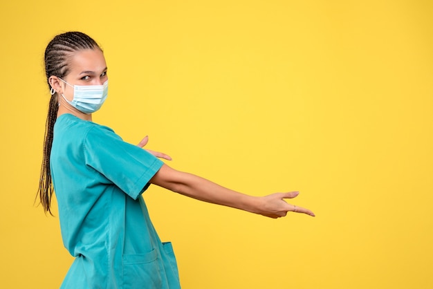 Vorderansicht der Ärztin im medizinischen Anzug und in der sterilen Maske auf gelber Wand