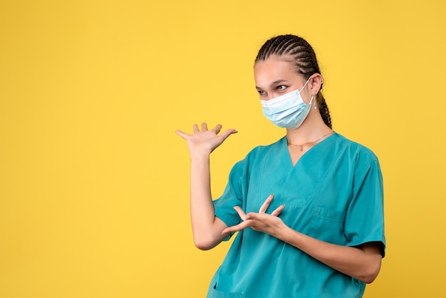 Vorderansicht der Ärztin im medizinischen Anzug und in der sterilen Maske auf gelber Wand