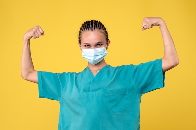 Vorderansicht der Ärztin im medizinischen Anzug und in der sterilen Maske, die auf gelber Wand biegt