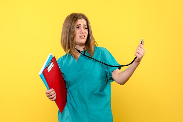 Vorderansicht der Ärztin mit Tonometer und Akten auf gelber Bodenfarbe Krankenhausmedizin