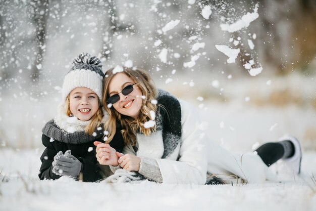 Vorderansicht der schönen Mutter und ihrer kleinen entzückenden Tochter, die auf dem Schnee liegt