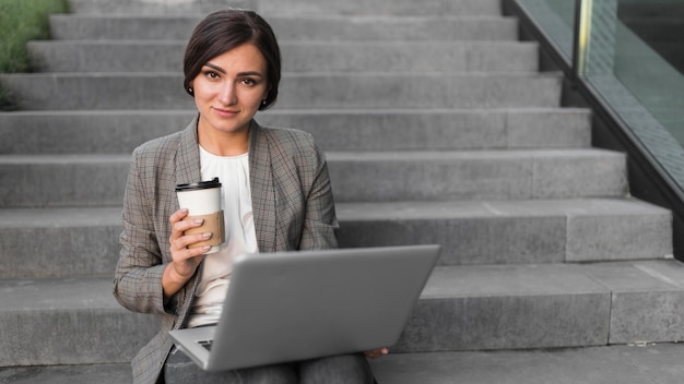 Kostenloses Foto vorderansicht der smiley-geschäftsfrau, die am laptop auf stufen arbeitet