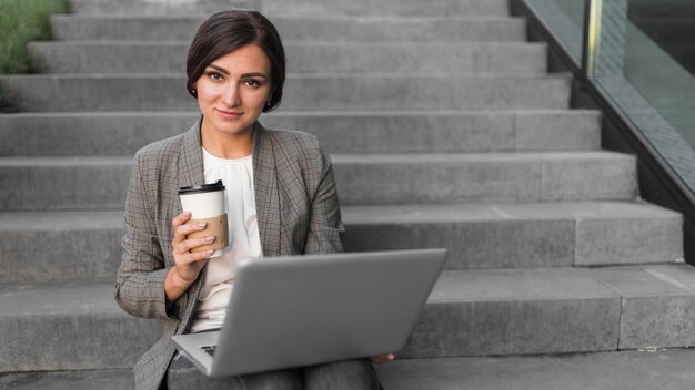 Vorderansicht der Smiley-Geschäftsfrau, die am Laptop auf Stufen arbeitet