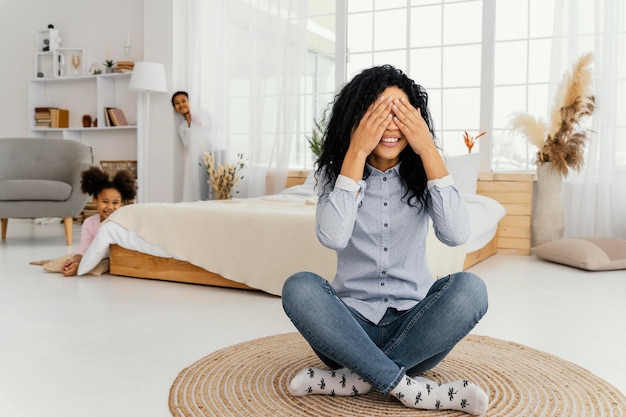 Kostenloses Foto vorderansicht der smiley-mutter, die verstecken mit ihren kindern zu hause spielt