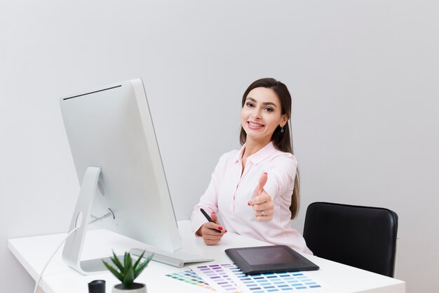 Vorderansicht der smileyfrau am Schreibtisch, der Daumen aufgibt