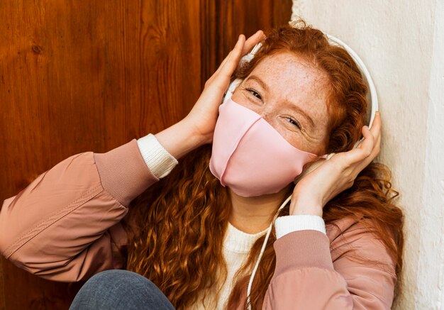 Kostenloses Foto vorderansicht der smileyfrau mit gesichtsmaske im freien und kopfhörern