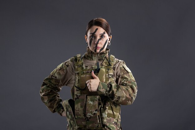 Vorderansicht der Soldatin in Militäruniform an dunkler Wand