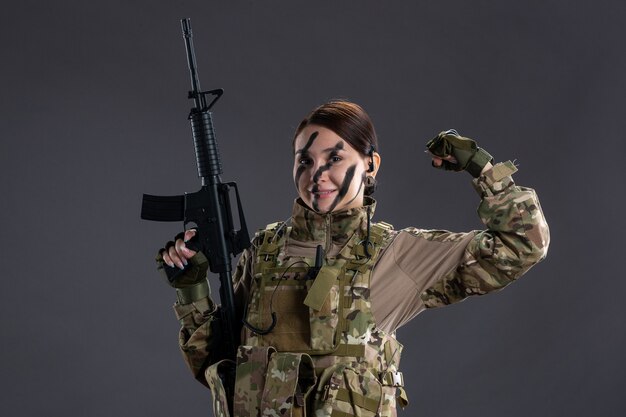 Vorderansicht der Soldatin in Tarnung mit Maschinengewehr an dunkler Wand