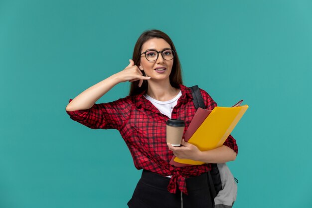 Vorderansicht der Studentin, die Rucksack hält, der Dateien und Kaffee an der blauen Wand hält