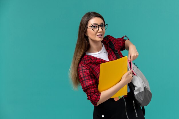 Vorderansicht der Studentin, die Rucksack trägt und Dateien an der hellblauen Wand hält