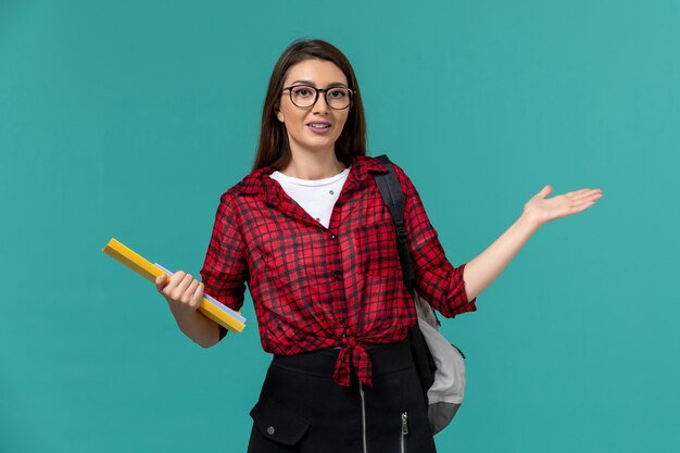 Vorderansicht der Studentin, die Rucksack trägt und Dateien an der hellblauen Wand hält