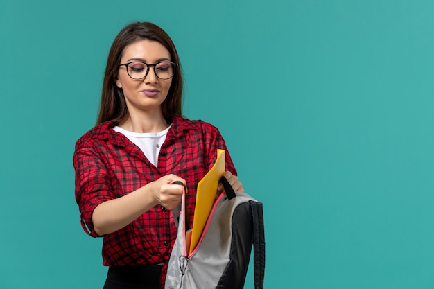 Vorderansicht der Studentin, die Rucksack und Akten an der hellblauen Wand hält