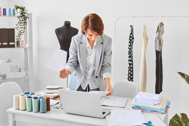 Vorderansicht der weiblichen Modedesignerin, die Kleidungslinienpläne im Atelier berät