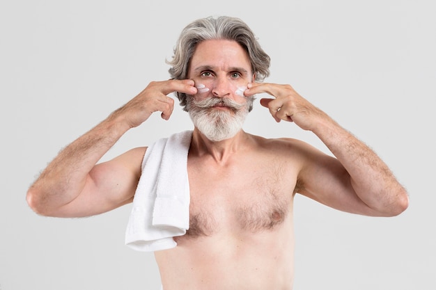 Vorderansicht des älteren Mannes mit Handtuch, das Feuchtigkeitscreme anwendet