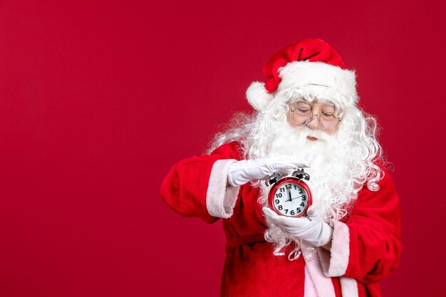 Vorderansicht des alten Weihnachtsmannes im roten Anzug mit Uhr an der roten Wand