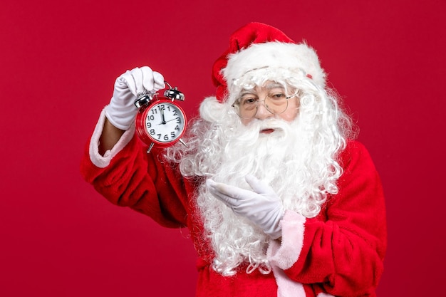 Vorderansicht des alten Weihnachtsmannes im roten Anzug mit Uhr an der roten Wand