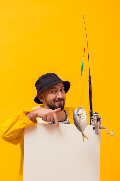 Vorderansicht des Fischers Angelrute halten und auf leeres Plakat zeigend