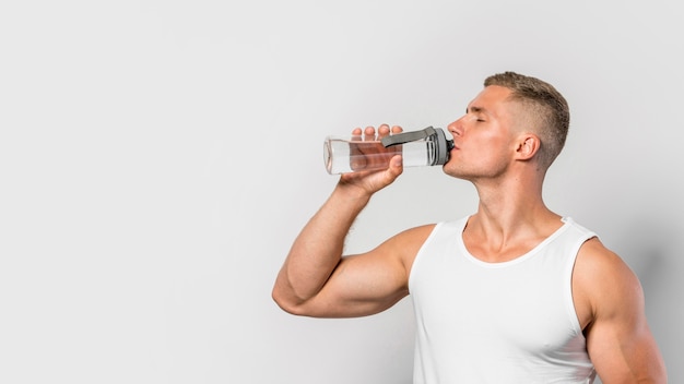 Vorderansicht des fitten Mannes, der von der Wasserflasche mit Kopienraum trinkt