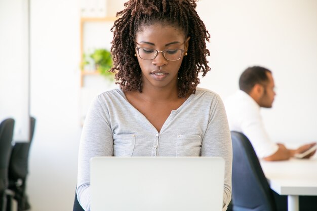 Vorderansicht des fokussierten weiblichen Angestellten, der auf Laptop schreibt