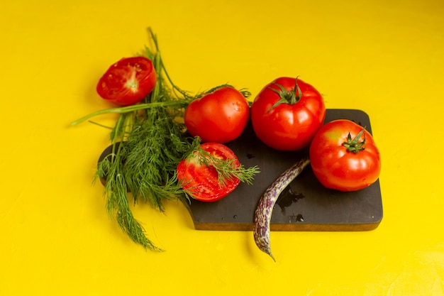 Vorderansicht des frischen und reifen Gemüses der frischen roten Tomaten mit Grün und Bohnen auf gelber Wand