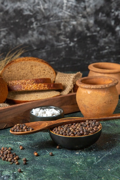 Vorderansicht des ganzen und geschnittenes frisches schwarzbrot auf handtuch in einer braunen holzkiste töpfereigewürze auf dunkler mischfarbenoberfläche