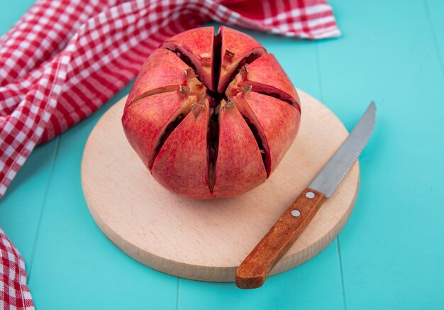 Vorderansicht des geschnittenen Granatapfels auf einem Schneidebrett mit einem Messer und einem rot karierten Handtuch auf einer blauen Oberfläche