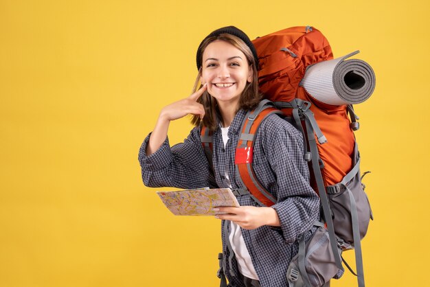 Vorderansicht des glücklichen jungen Reisenden mit Rucksack, der Karte zeigt, die auf ihr Lächeln zeigt