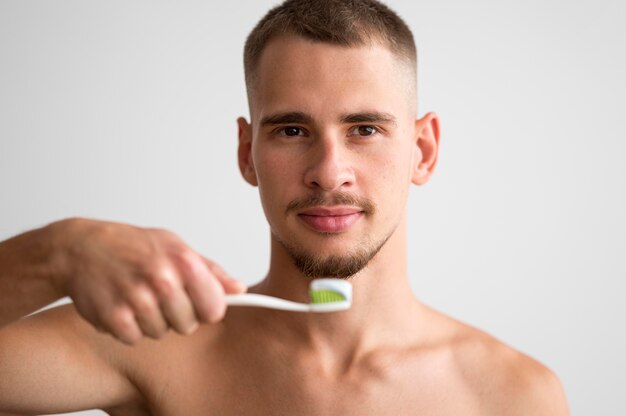 Vorderansicht des gutaussehenden Mannes, der Zahnbürste mit Zahnpasta auf ihm hält