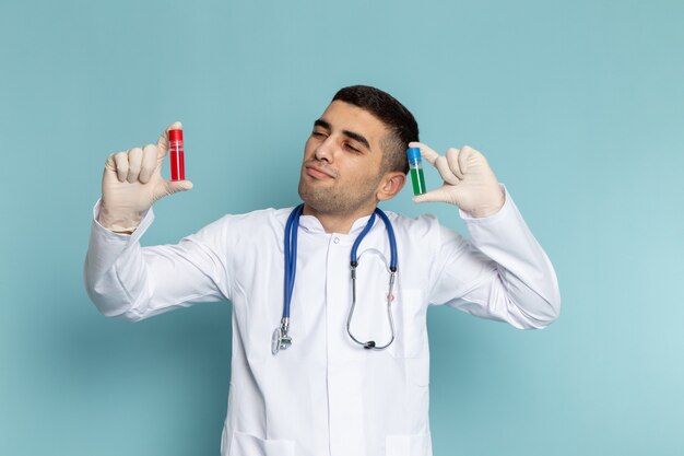 Vorderansicht des jungen männlichen Arztes im weißen Anzug mit blauen Stethoskop-Halteflaschen